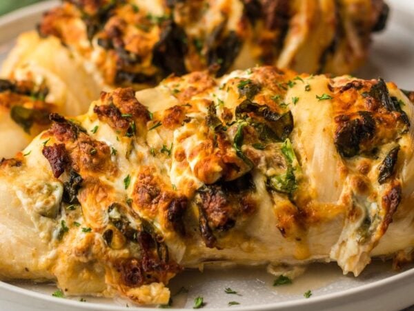 Stuffed chicken breast with herbs and melted cheese on a white plate—an irresistible air fryer chicken recipe inspired by creamy bacon chicken.