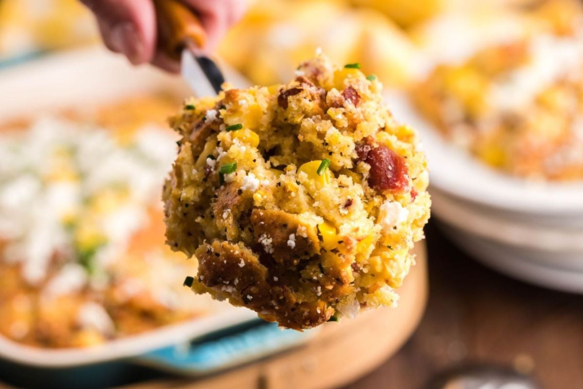 A close-up of a spoonful of cheesy corn casserole with bacon and herbs.
