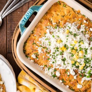 Baked Mexican street corn casserole made with Jiffy cornbread mix, topped with cheese, herbs, and corn in a dish on a wooden table.