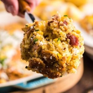 A close-up of a spoonful of cheesy corn casserole with bacon and herbs.