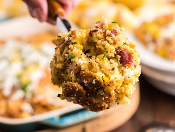 A close-up of a spoonful of cheesy corn casserole with bacon and herbs.