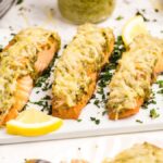 Baked salmon fillets topped with pesto and melted cheese, inspired by Air Fryer Parmesan Pesto Salmon, garnished with lemon wedges and herbs on a white plate.