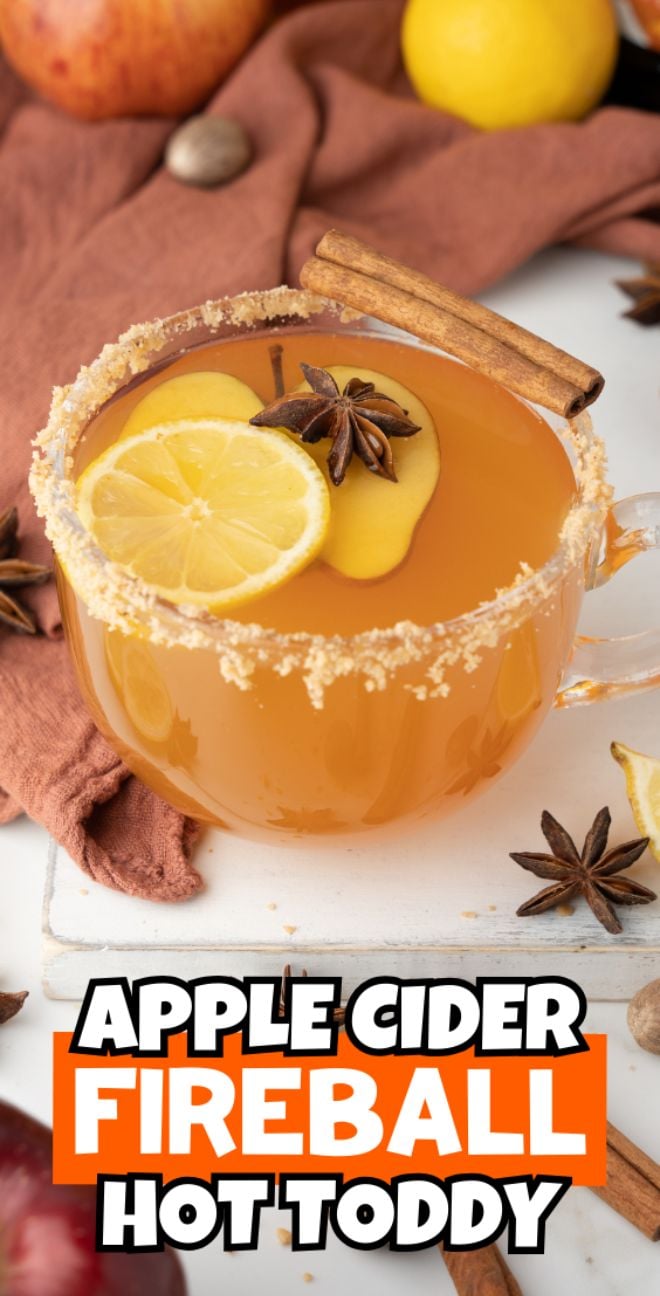 A glass mug of caramel apple hot toddy with lemon, star anise, and a cinnamon stick, rimmed with sugar.