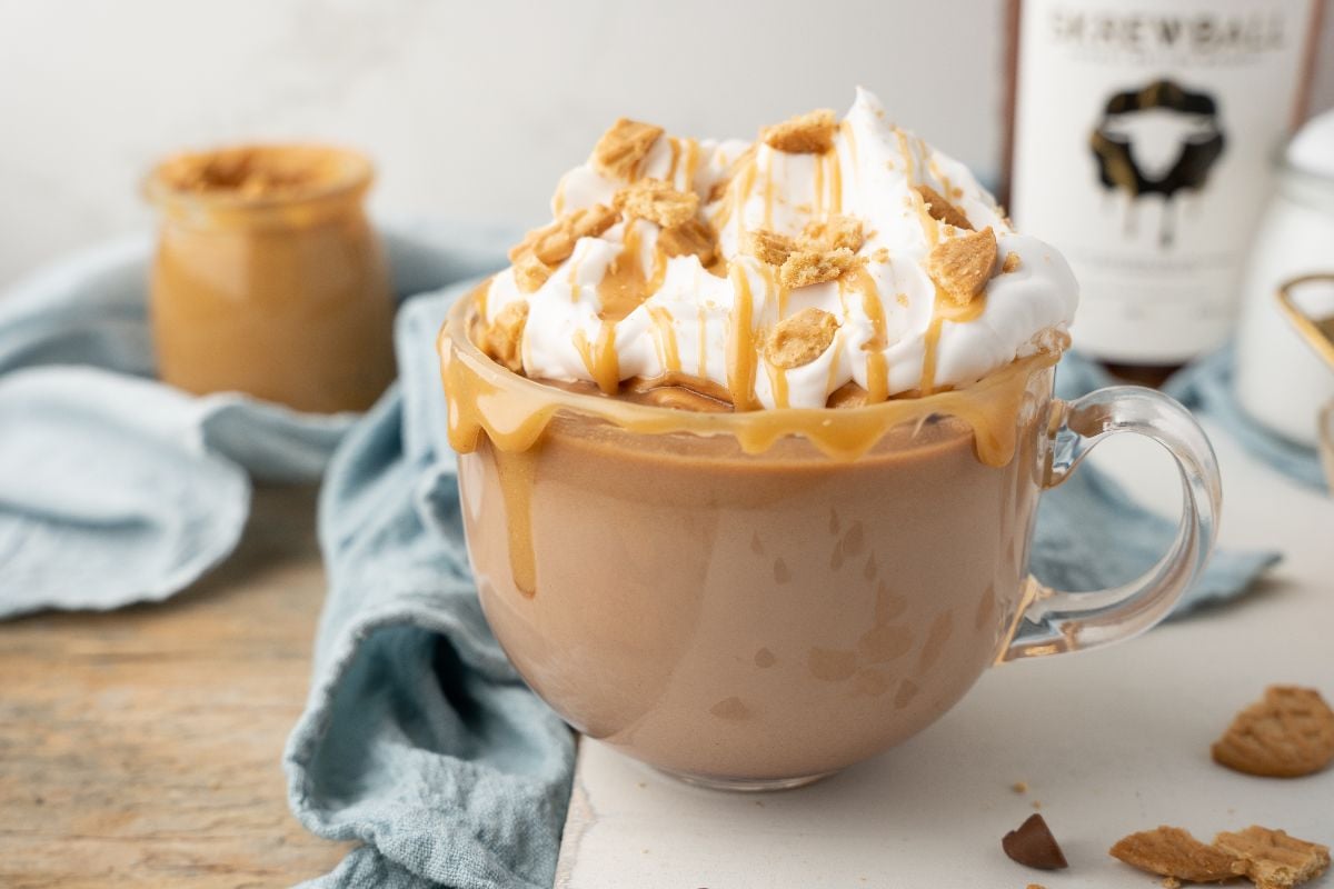 A glass mug of hot chocolate and whiskey topped with whipped cream, caramel drizzle, and cookie crumbles.