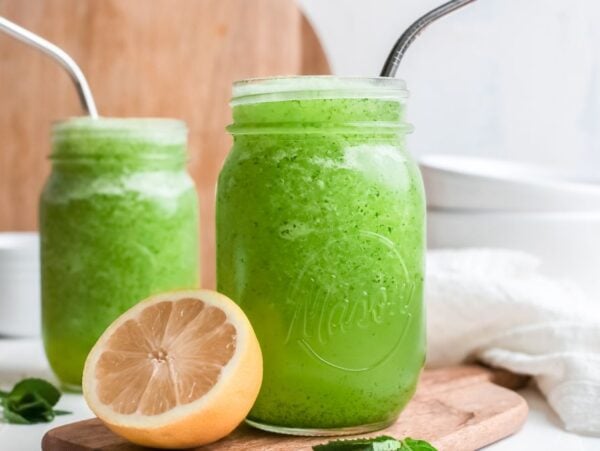 Two mason jars filled with a refreshing Limonana—an icy lemon and mint drink—sit with metal straws and a halved lemon on a wooden board.