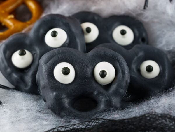 Black Halloween Monster Eye Pretzels decorated with candy eyes, arranged on a spooky cobweb background—an eerie and fun Halloween snack for kids.