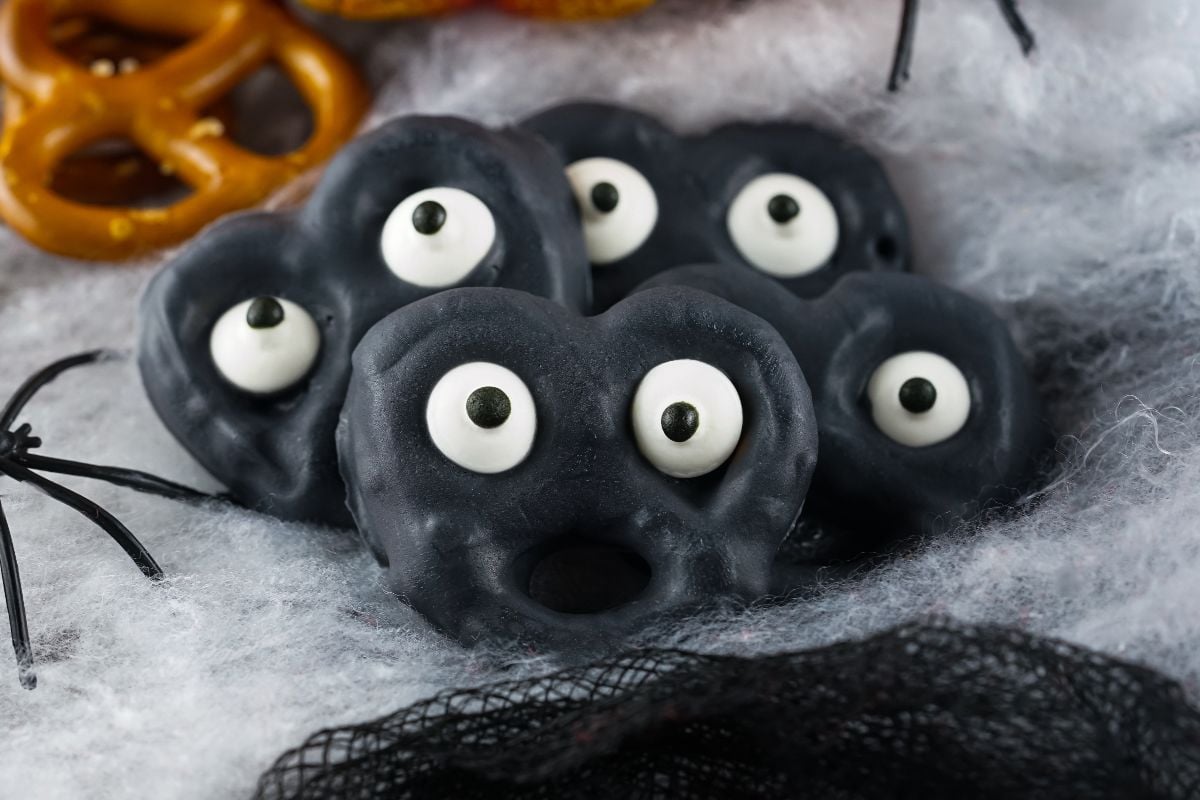 Black candy-coated pretzels with candy eyes on fake spiderweb, these Halloween pretzels with eyeballs make spooky monster treats perfect for any party table.