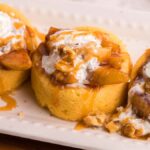 Three mini fireball apple shortcake dessert cups topped with whipped cream, caramel sauce, apple slices, and chopped walnuts make a delightful treat on a white plate.