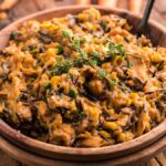 A wooden bowl of creamy instant pot wild rice and lentil casserole, garnished with fresh herbs on top.