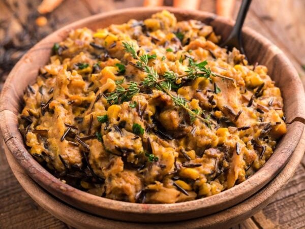 A wooden bowl of creamy instant pot wild rice and lentil casserole, garnished with fresh herbs on top.