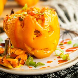 A stuffed orange bell pepper carved like a jack o lantern, served on a plate with sauce and green onions—perfect as a fun Halloween dinner recipe or festive food to eat on Halloween.