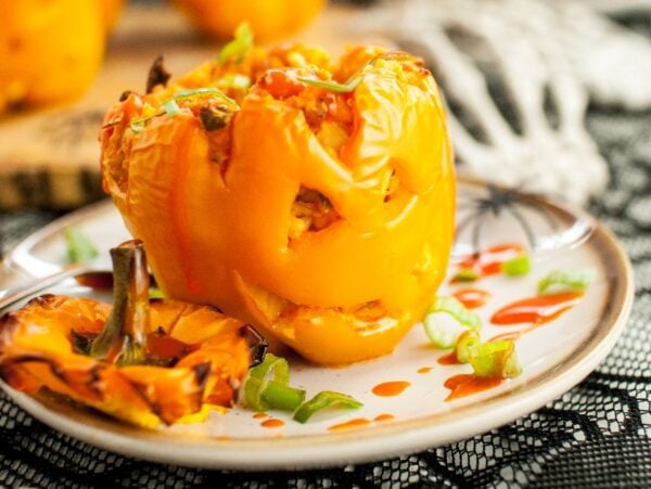 A stuffed orange bell pepper carved like a jack o lantern, served on a plate with sauce and green onions—perfect as a fun Halloween dinner recipe or festive food to eat on Halloween.