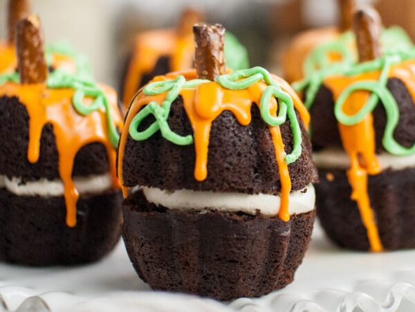 Chocolate cupcakes decorated like pumpkins with orange icing, green vines, and pretzel stick stems—perfect as a Thanksgiving or Halloween dessert or for learning how to make a pumpkin shaped cake.