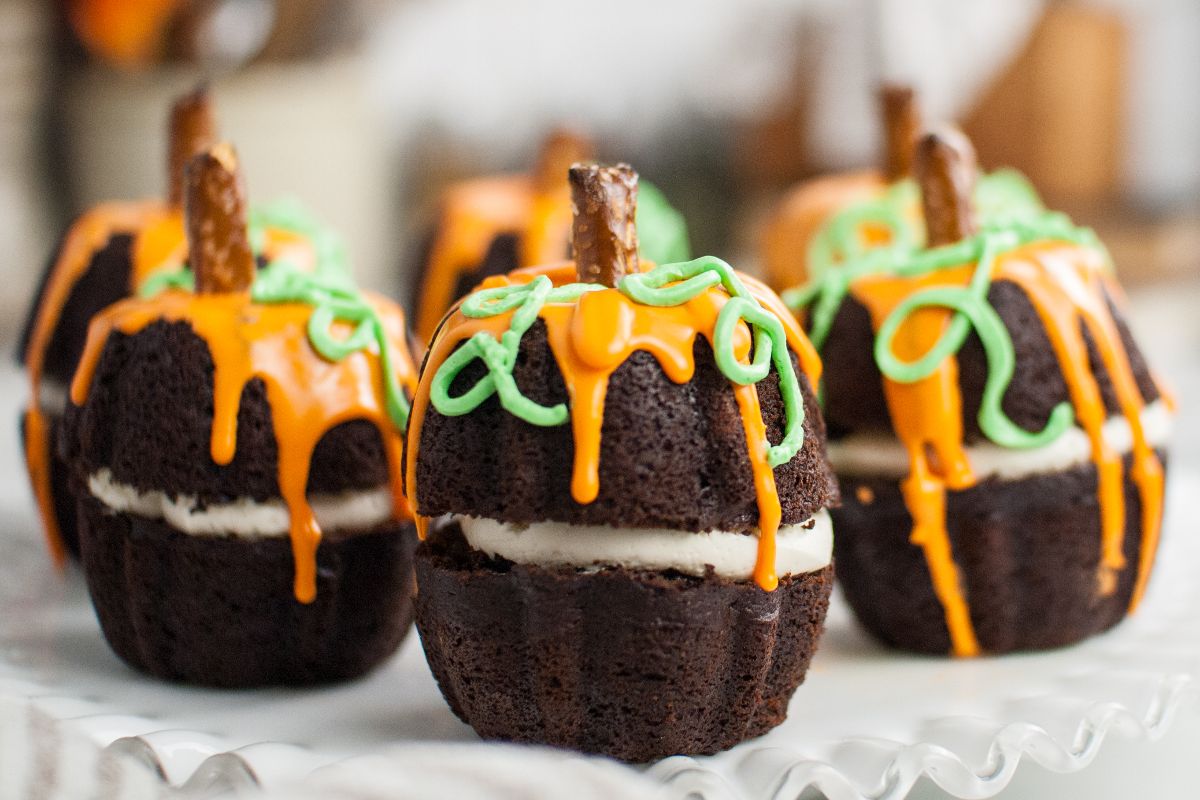 Chocolate cupcakes decorated as pumpkins with orange and green icing and a pretzel stem—perfect mini Halloween pumpkin cakes for your spooky celebration.