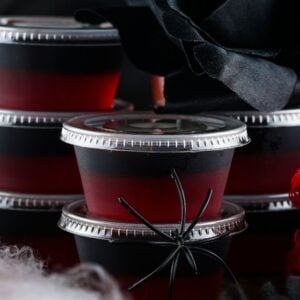 Stacked black and red layered jelly cups with plastic spider, apple, and black rose make spooky Halloween decor—perfect inspiration if you're learning how to make Halloween jello shots like Vampire Kiss Jello Shots.