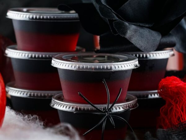 Stacked black and red layered jelly cups with plastic spider, apple, and black rose make spooky Halloween decor—perfect inspiration if you're learning how to make Halloween jello shots like Vampire Kiss Jello Shots.