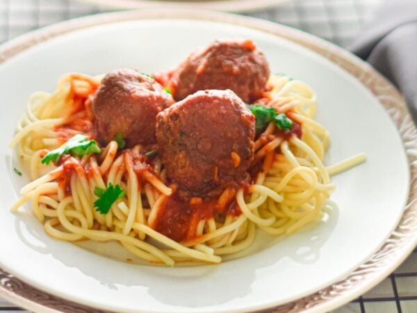 Spaghetti topped with gluten free air fryer meatballs, marinara sauce, and parsley on a white plate with a silver rim.