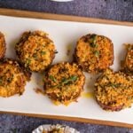 Eight breaded, baked stuffed mushrooms topped with herbs, served on a white rectangular plate with basil garnish—perfect alongside crisp Air Fryer Sweet Potato Stacks for a delightful appetizer duo.