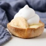 Mini Banana Cream Pie topped with whipped cream, made with pre-made pie crust and instant vanilla pudding, sits on a light surface with a blue cloth in the background.