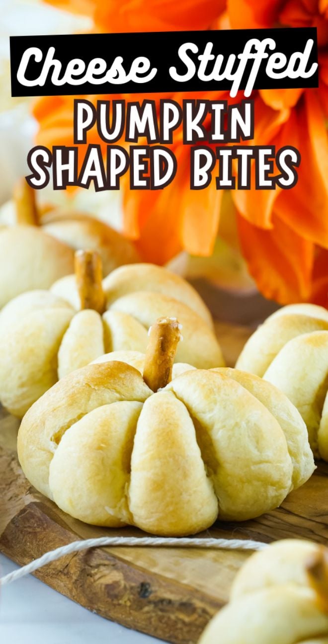 Cheese Stuffed Pumpkin Shaped Bites wrapped in Pillsbury crescent roll dough with pretzel stems sit on a wooden board, orange flowers in the background—a festive snack for Thanksgiving or Halloween.
