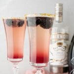 Two Lemon Berry Prosecco Cocktails in flutes, featuring lemon vodka and Meyer lemon blackberry syrup, with bottles of vodka and sparkling wine in the background.