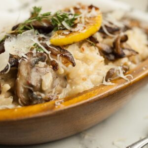 Creamy mushroom risotto in a wooden bowl, topped with grated cheese, mushrooms, lemon slice, and herbs—a simple risotto recipe enhanced with a splash of white wine for extra depth and flavor.