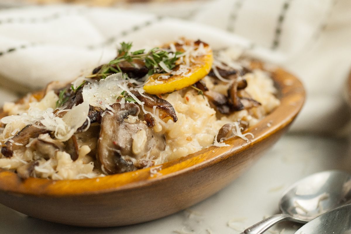 Creamy mushroom risotto topped with herbs, lemon slice, and grated cheese in a wooden bowl—a simple risotto recipe enhanced with white wine, perfect as a side dish for chicken or turkey.