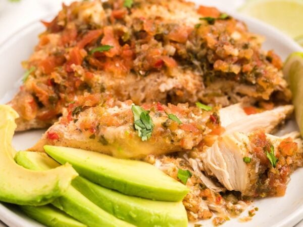 Baked chicken breasts topped with salsa, served with avocado slices and lime wedges on a white plate—an easy keto chicken recipe perfect for a quick meal.