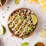 A bowl of southwest inspired taco salad topped with diced veggies, lettuce, creamy dressing, and a lime wedge sits on a marble table.