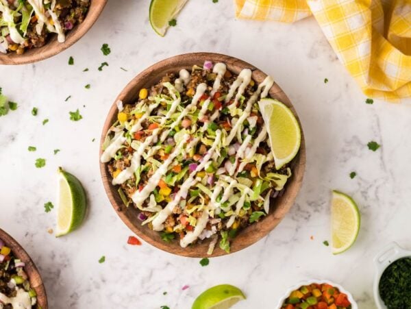 A bowl of southwest inspired taco salad topped with diced veggies, lettuce, creamy dressing, and a lime wedge sits on a marble table.