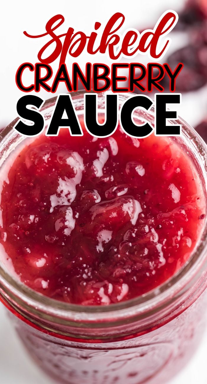 Open jar of red cranberry sauce with "Spiked Cranberry Sauce" written above in bold red and black text, highlighting a spiked cranberry sauce recipe perfect for the holidays.