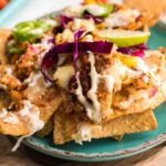 A plate of nachos topped with shredded chicken, red cabbage, jalapeños, lime, and creamy sauce—perfect for trying new topping ideas or as inspiration for your next seafood nachos recipe.