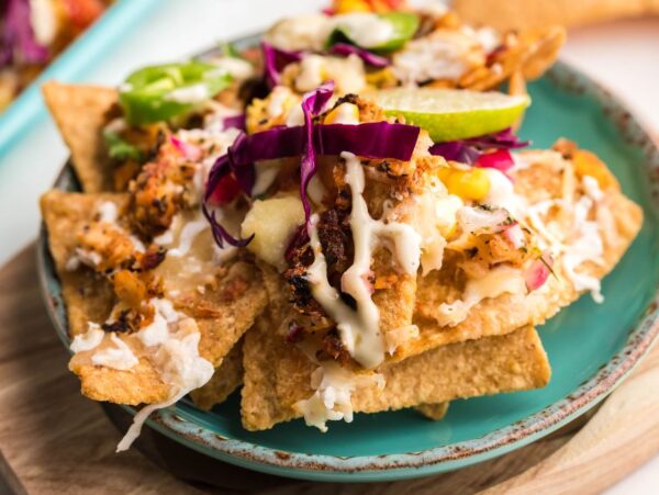 A plate of nachos topped with shredded chicken, red cabbage, jalapeños, lime, and creamy sauce—perfect for trying new topping ideas or as inspiration for your next seafood nachos recipe.
