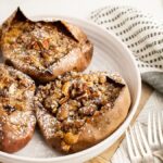 Three Twice Baked Sweet Potatoes topped with streusel and pecans on a white plate, dusted with powdered sugar.