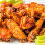 Plate of saucy Air Fryer Peach-Bourbon Wings with celery sticks on a white dish.