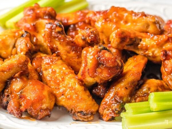 Plate of saucy Air Fryer Peach-Bourbon Wings with celery sticks on a white dish.