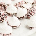 Dipped meringue kisses coated in chocolate and crushed peppermint, with candy canes on white parchment paper—a festive treat for christmas meringue cookie recipes.
