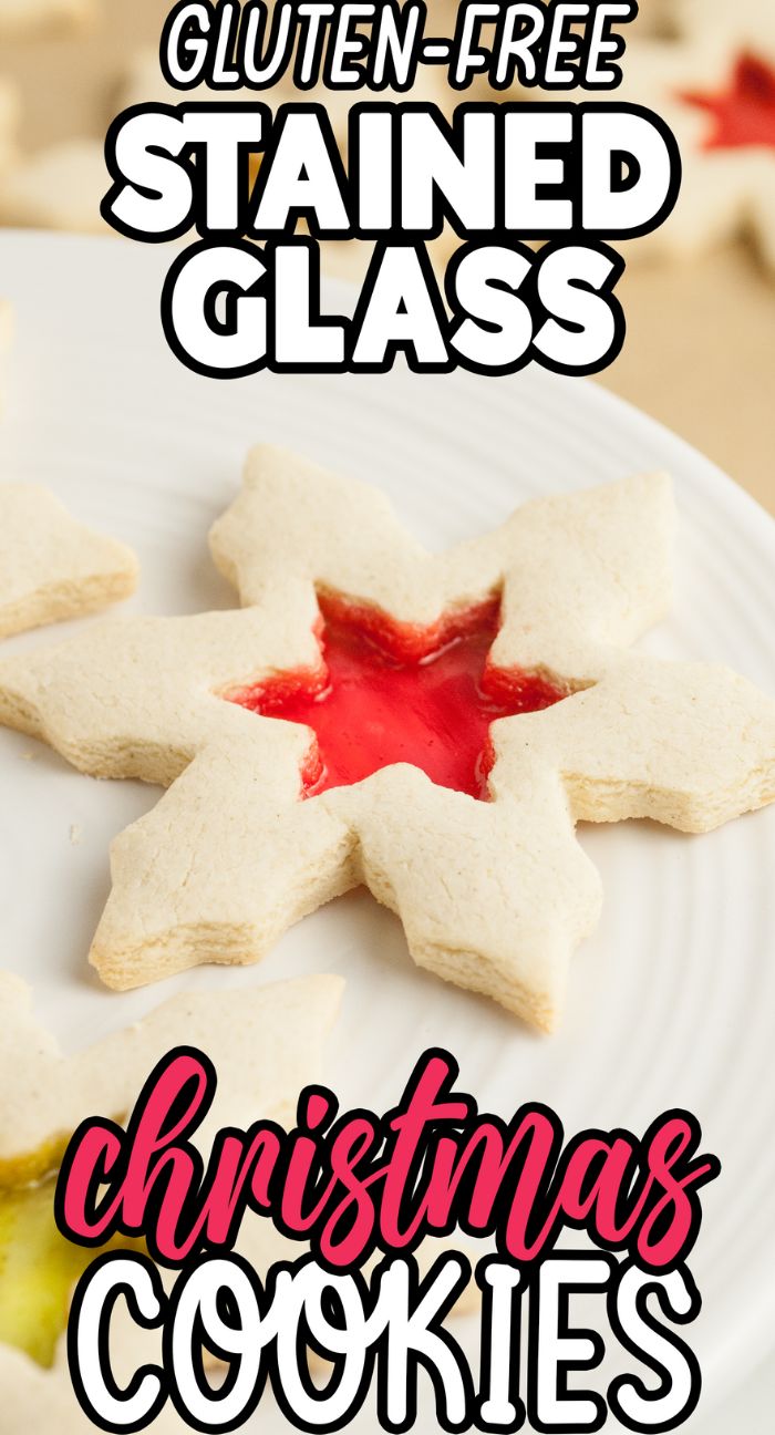 Snowflake-shaped Gluten Free Stained Glass Christmas Cookies with a red hard candy center shine on a white plate. These festive cookies with a hole in the middle are labeled gluten-free Christmas cookies.