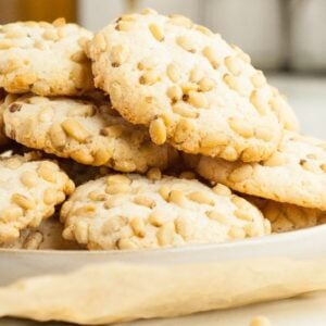 A plate of almond and pine nut cookies stacked on parchment paper, with a blurred background—perfect for easy gluten free holiday baking.