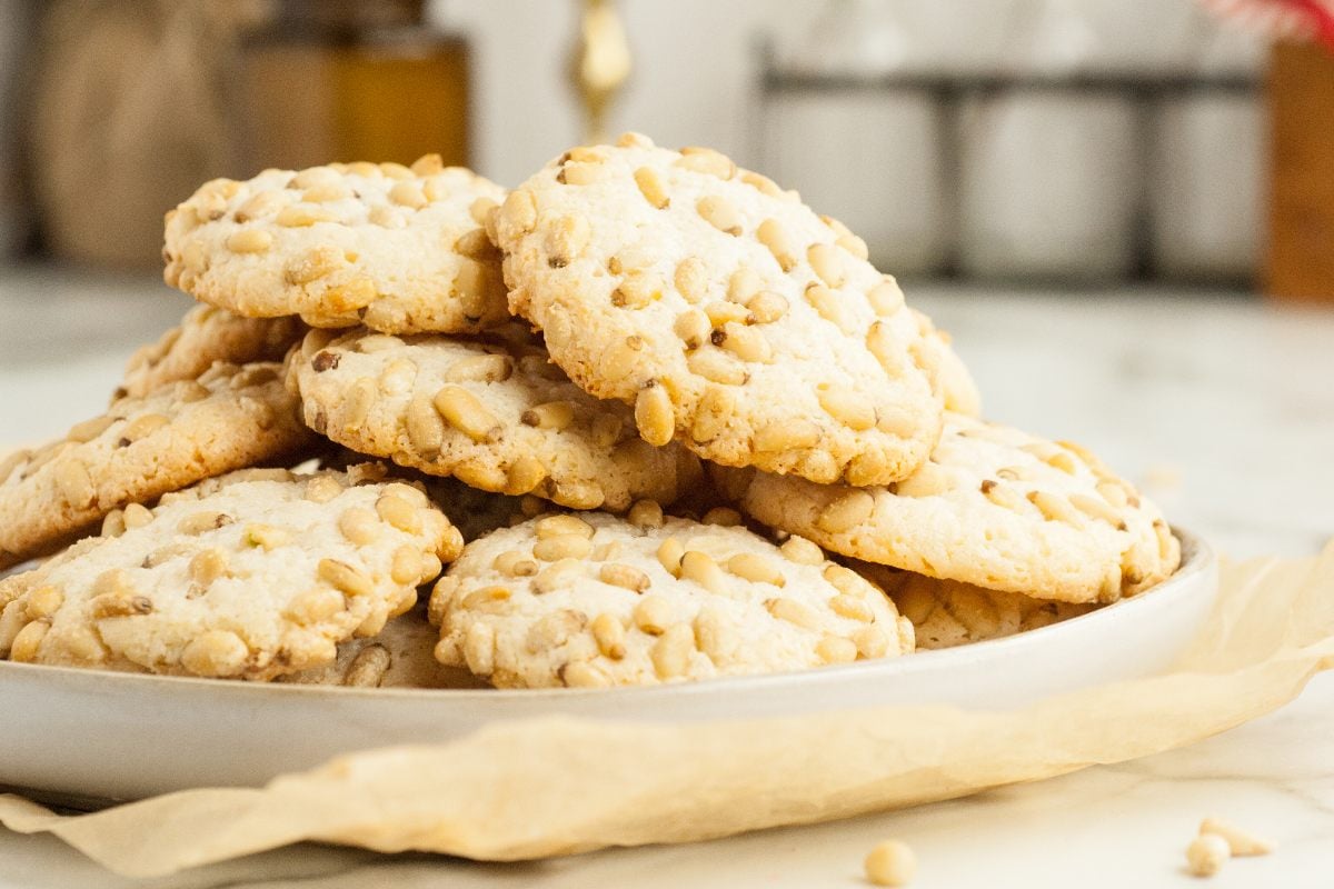 A plate of almond and pine nut cookies, inspired by the classic Italian Pignoli cookie recipe, stacked on parchment paper.