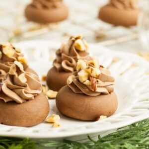 Italian Nutella cookies topped with swirls of chocolate cream and chopped nuts sit on a white plate, garnished with fresh greens.