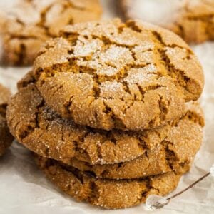 A stack of sugar-coated Starbucks Copycat Ginger Molasses Cookies on parchment paper, with more cookies in the background.