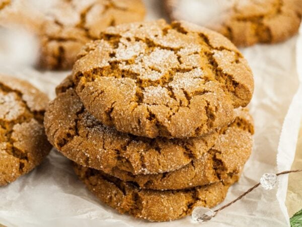 A stack of sugar-coated Starbucks Copycat Ginger Molasses Cookies on parchment paper, with more cookies in the background.