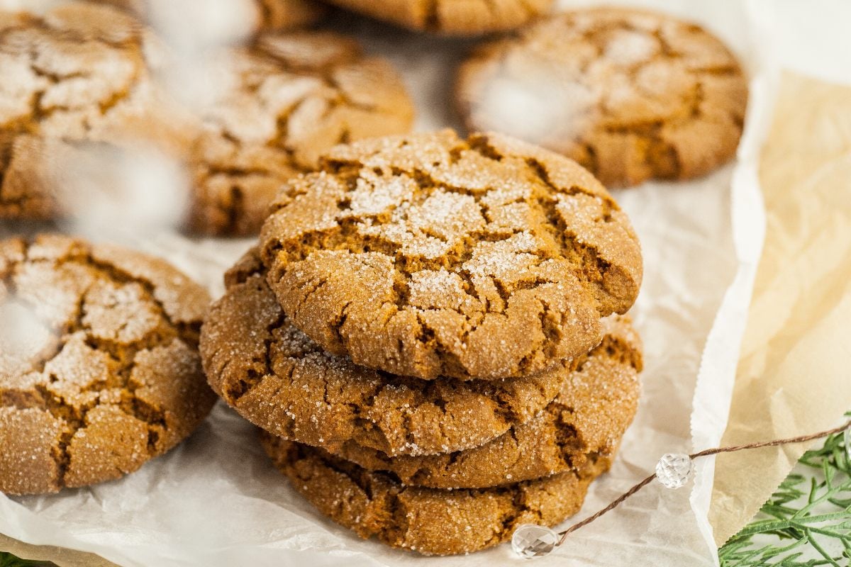 A stack of three Starbucks Copycat Ginger Molasses Cookies on parchment paper with more cookies in the background.