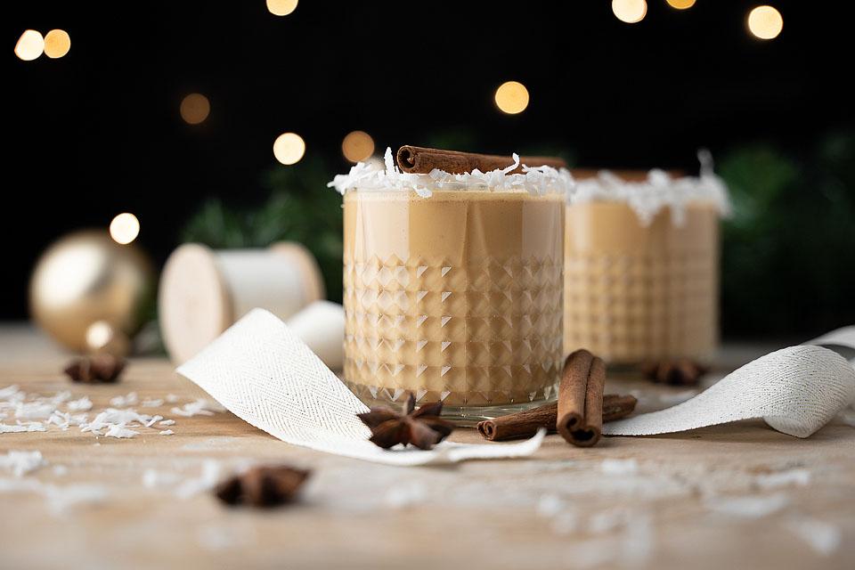 Two cups of eggnog with cinnamon sticks on a wooden table.