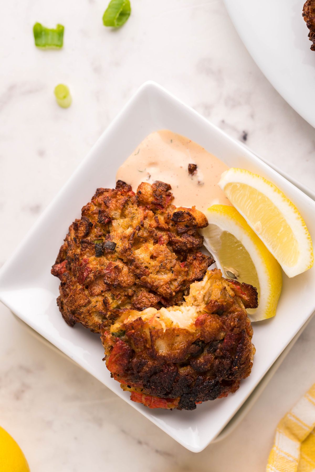Two southwest crab cakes on a white plate with lemon wedges and a side of creamy, spicy sauce for crab cakes.