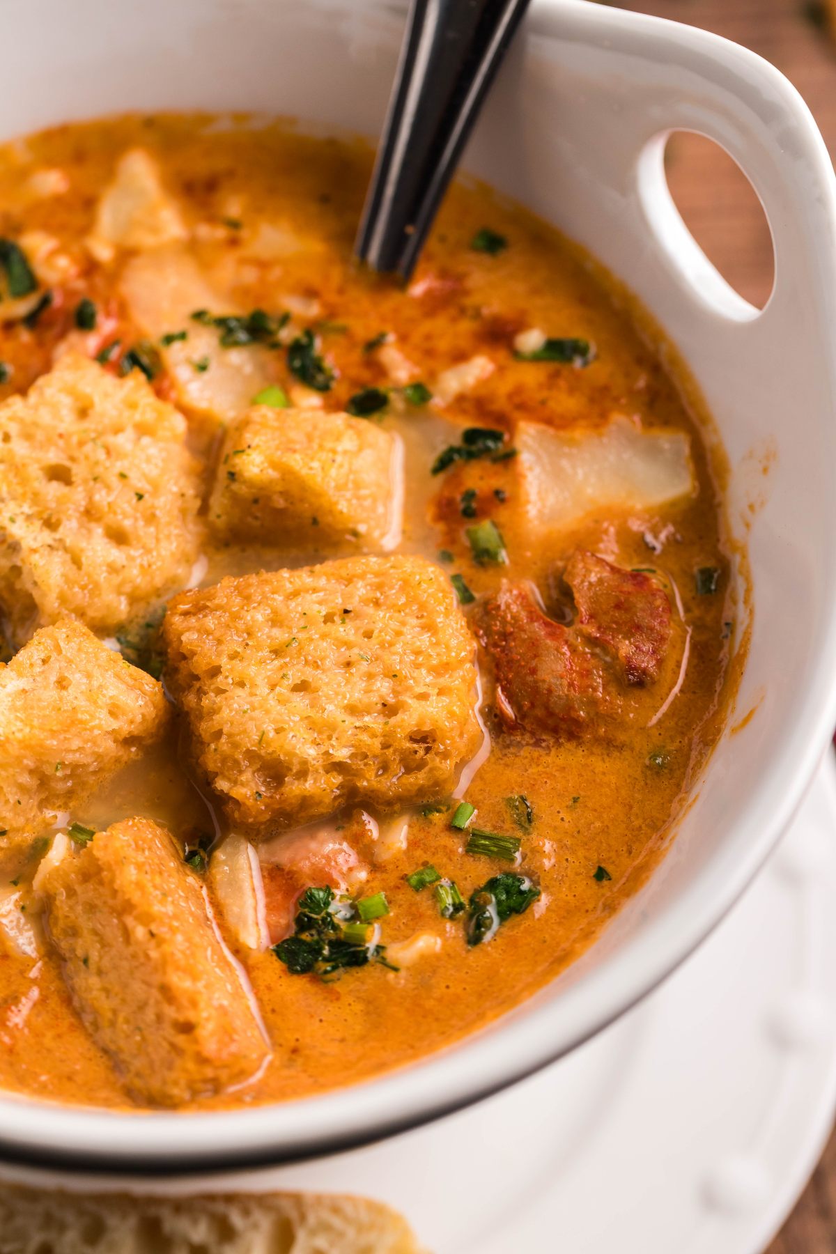 Creamy Slow Cooker Seafood Bisque with croutons and herbs, served in a white bowl on a plate with a spoon.