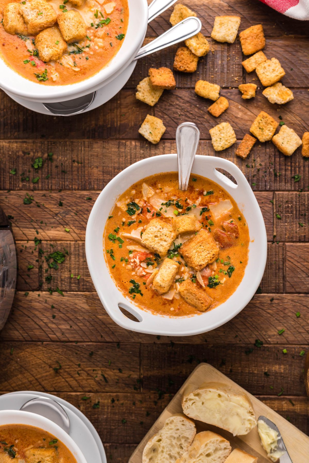 Bowls of creamy seafood soup, like a Slow Cooker Seafood Bisque, topped with croutons and served with bread on a rustic wooden table.