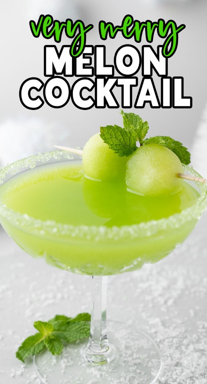 A bright Grinch green Christmas cocktail with melon balls and mint garnish, served in a sugar-rimmed glass.