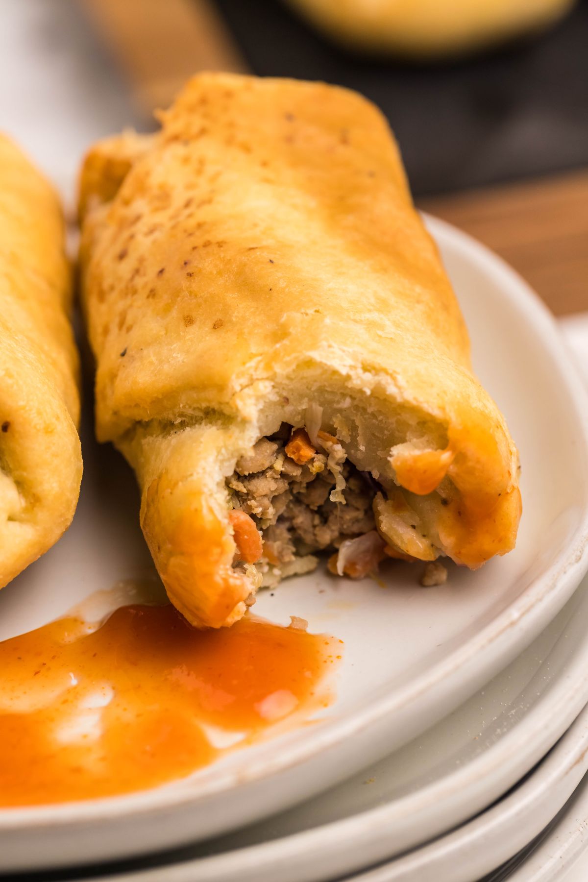 Half-eaten stuffed bread roll with meat and vegetables, made using Air Fryer Gluten Free Egg Roll Wrappers, served on a plate with orange dipping sauce.